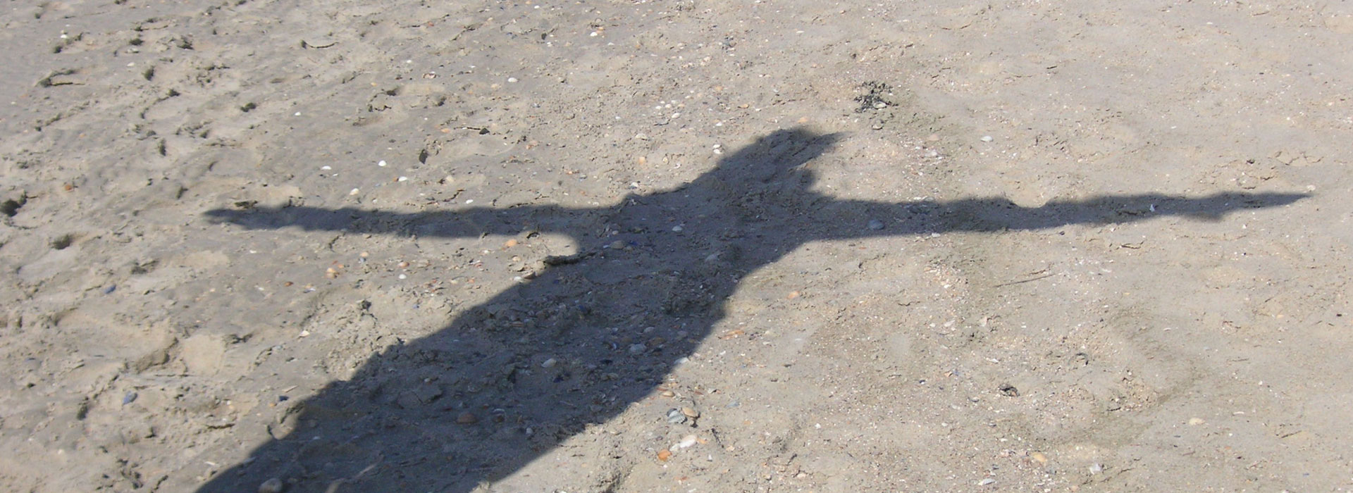 Der Schatten einer Person am Strand wurde mit ausgebreiteten Armen fotografiert. Es sieht aus wie ein Engel mit Flügeln.
